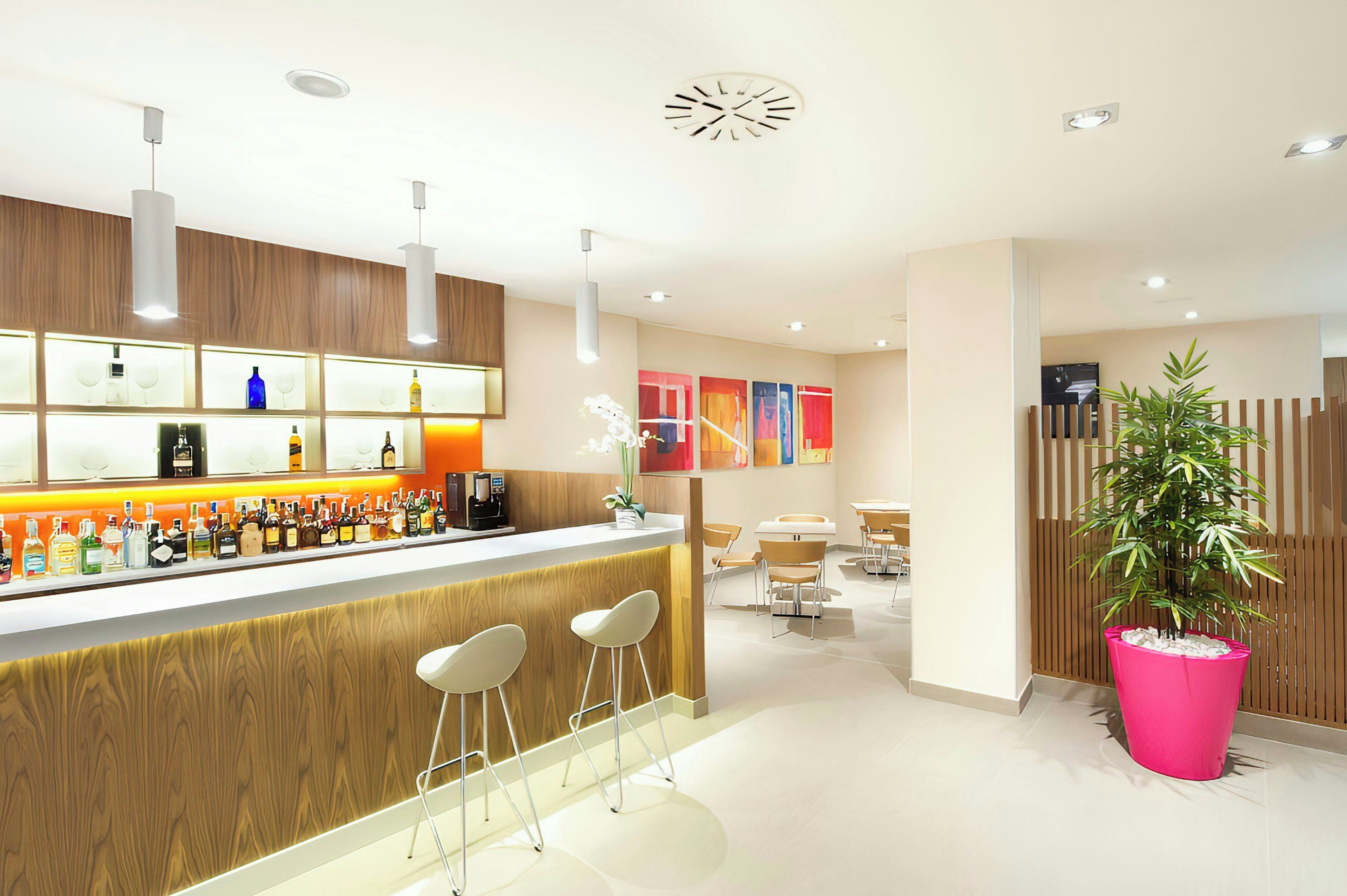 A modern bar area with a wooden counter, bar stools, and a variety of bottles.