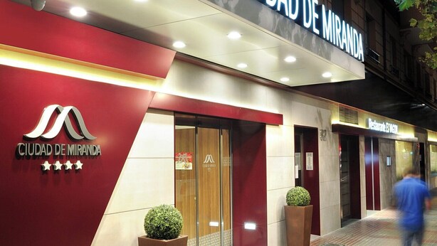 Exterior del Hotel Ciudad de Miranda con un cartel llamativo, fachada roja y un camino de ladrillos.
