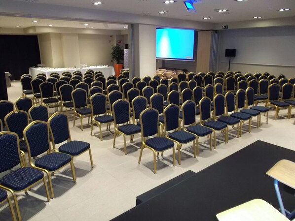 Un salón de conferencias con hileras de sillas azules y un escenario.