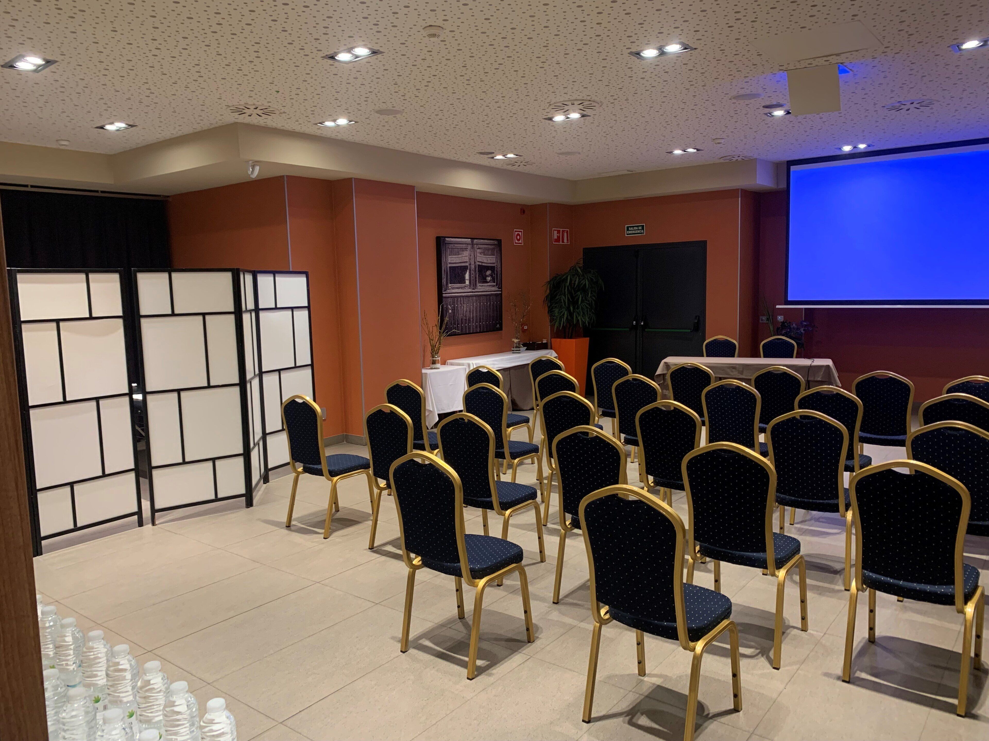 A conference room with rows of chairs, a projector screen, a whiteboard, and a blackboard.
