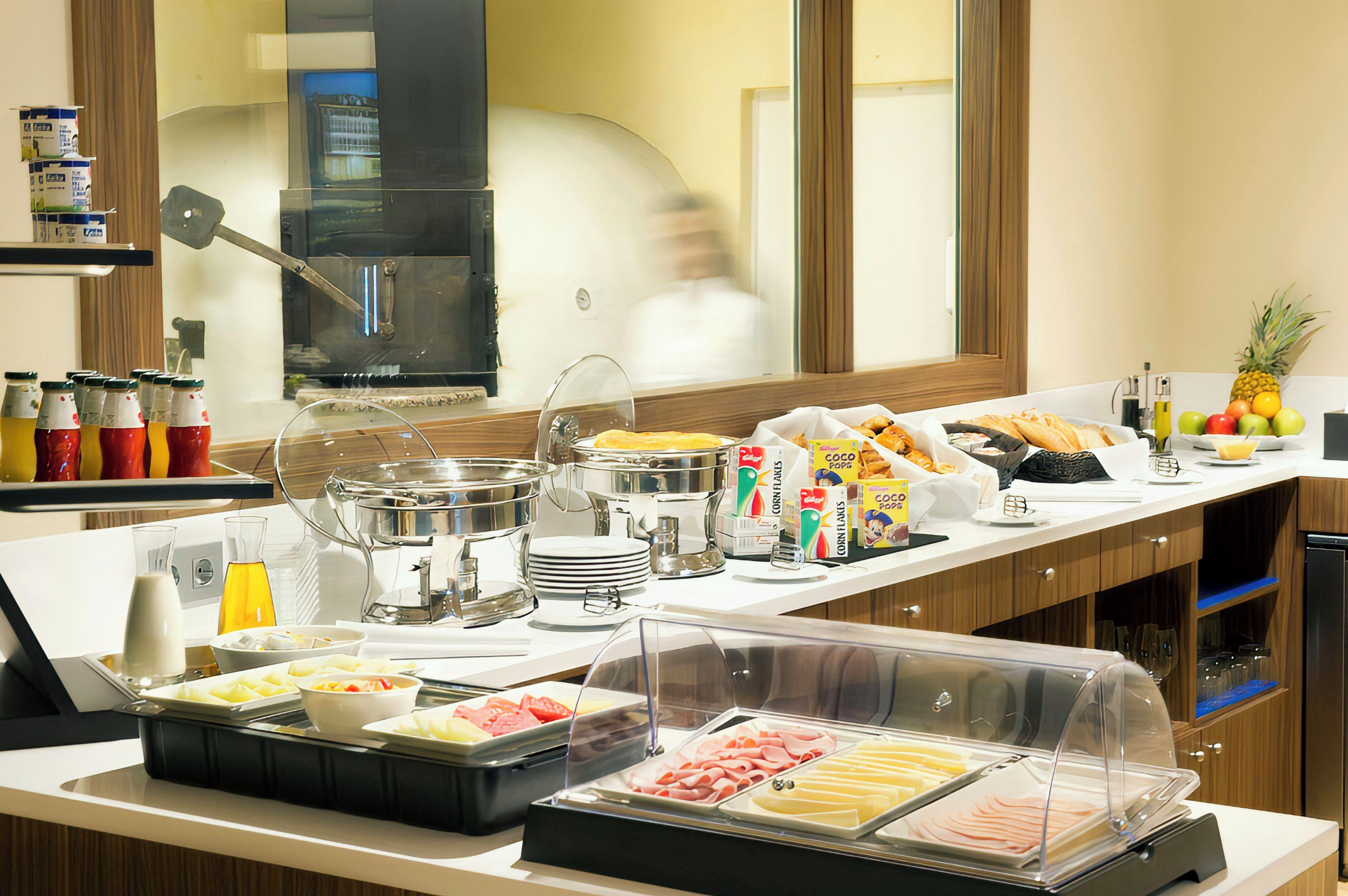 Un bufé con diversas opciones de comida, entre ellas frutas, cereales y carnes, en un entorno hotelero.