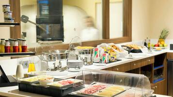 Un bufé con diversas opciones de comida, entre ellas frutas, cereales y carnes, en un entorno hotelero.