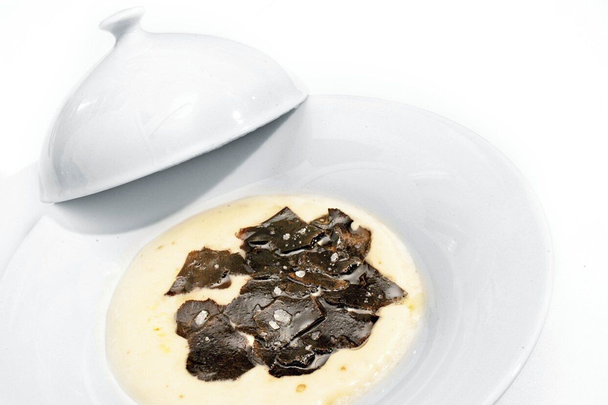 A white plate with a creamy substance and dark pieces on top, accompanied by a white lid.