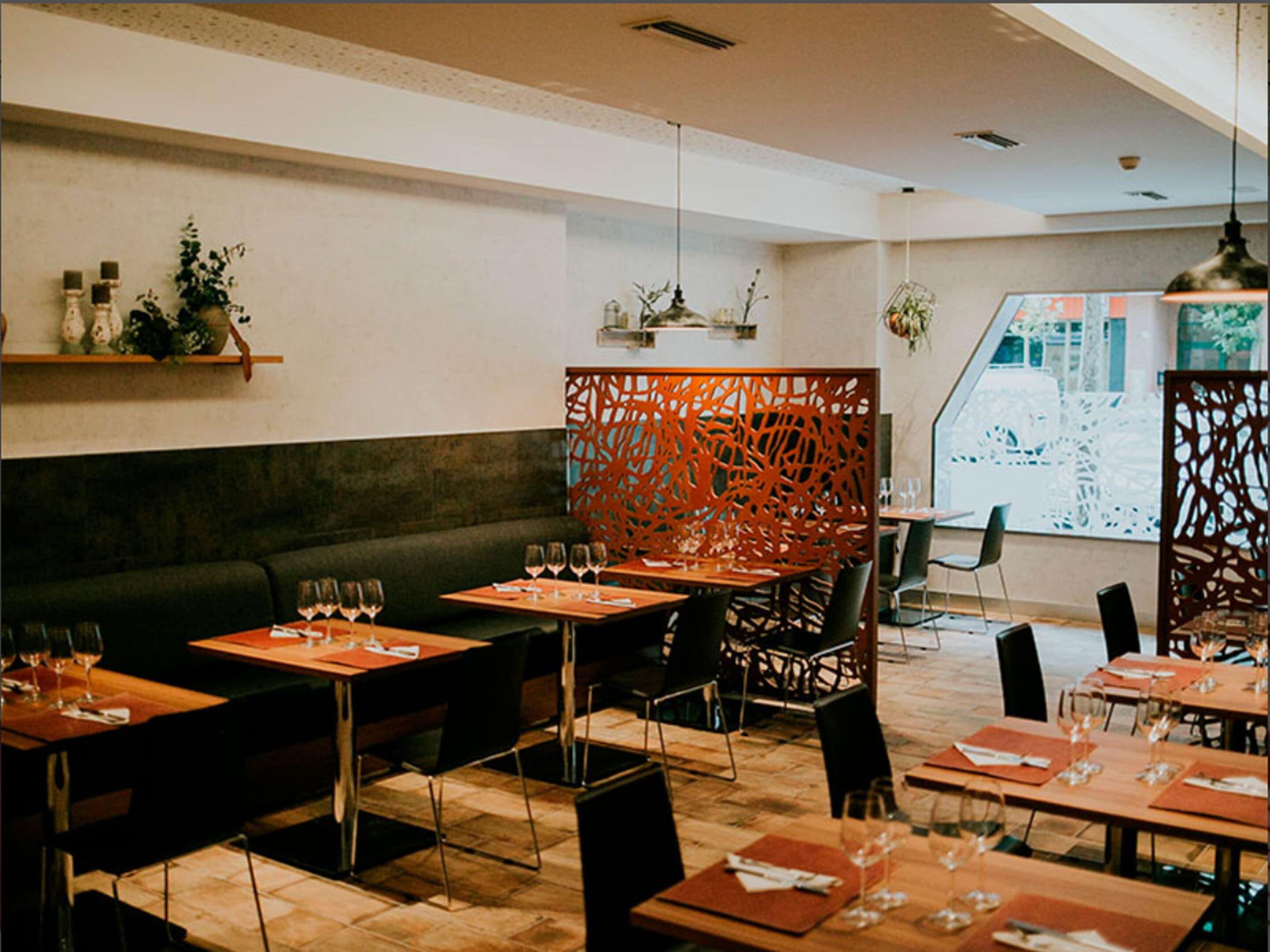 Un interior de restaurante con mesas de madera, sillas negras y un sofá verde.