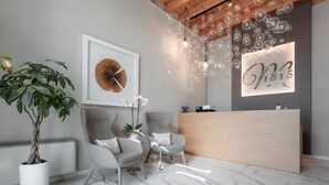 Un espace d’accueil doté d’un sol en marbre, de deux fauteuils gris, d’une plante en pot, d’une œuvre d’art encadrée et d’un comptoir de réception en bois sur lequel est apposée une enseigne.