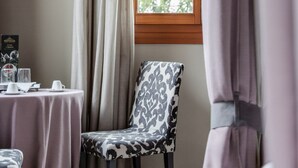 Une pièce avec une table dressée pour deux personnes, une chaise à motifs et une fenêtre avec des rideaux.