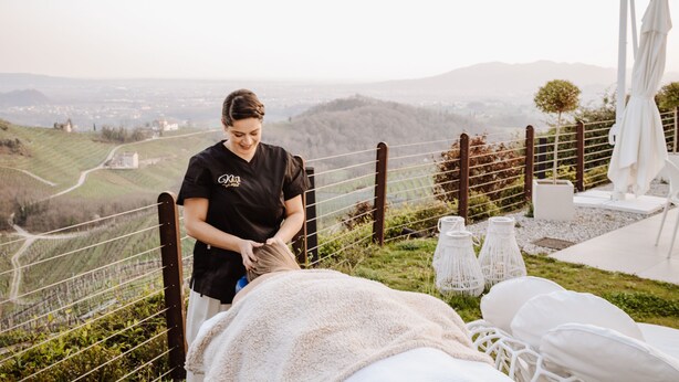 Une personne reçoit un massage en plein air, avec une vue panoramique sur des collines et une clôture en arrière-plan.