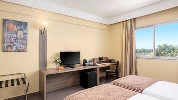 Habitación de hotel con cama, escritorio, televisor, refrigerador pequeño y ventana con vista.