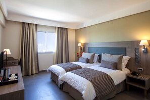 Una habitación de hotel con dos camas, un escritorio con lámpara y una mesita de noche con teléfono.