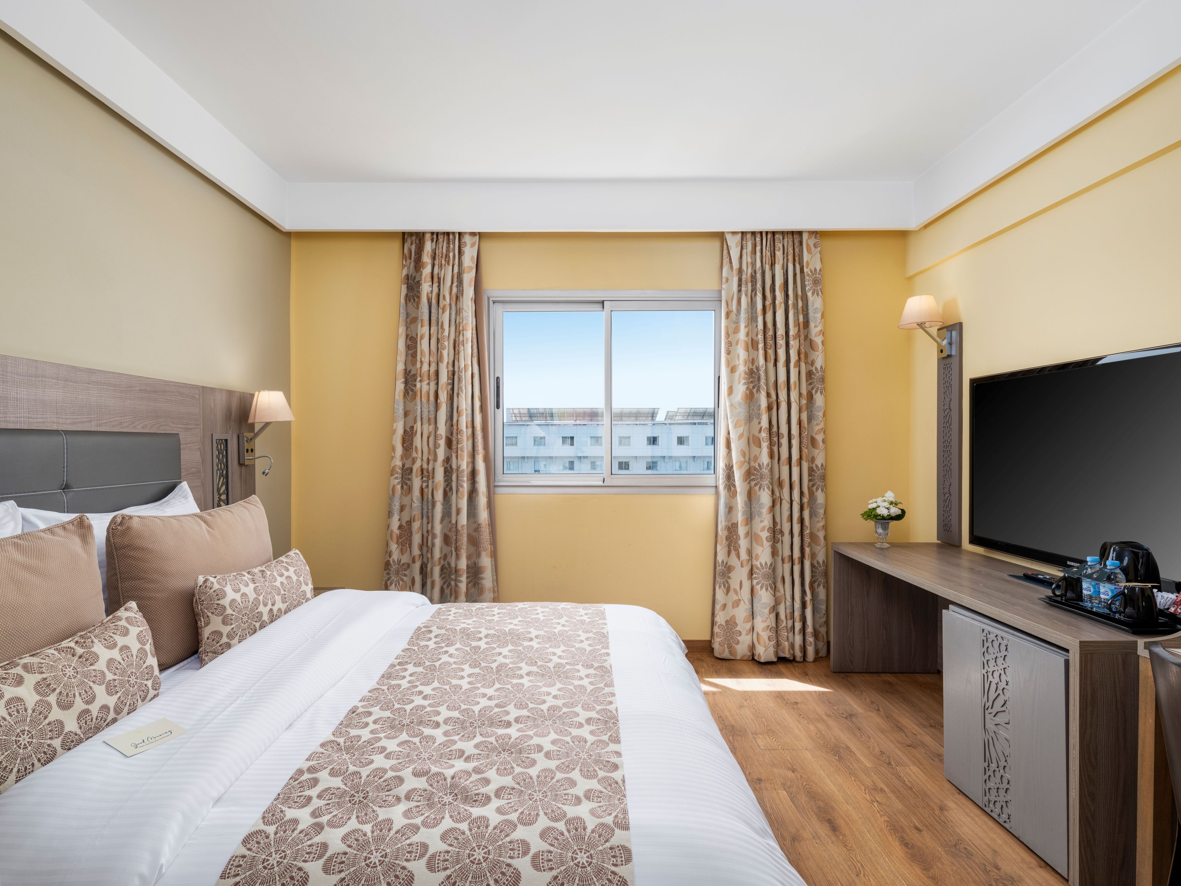 A hotel room with a bed, a television, a desk, and a window with curtains.