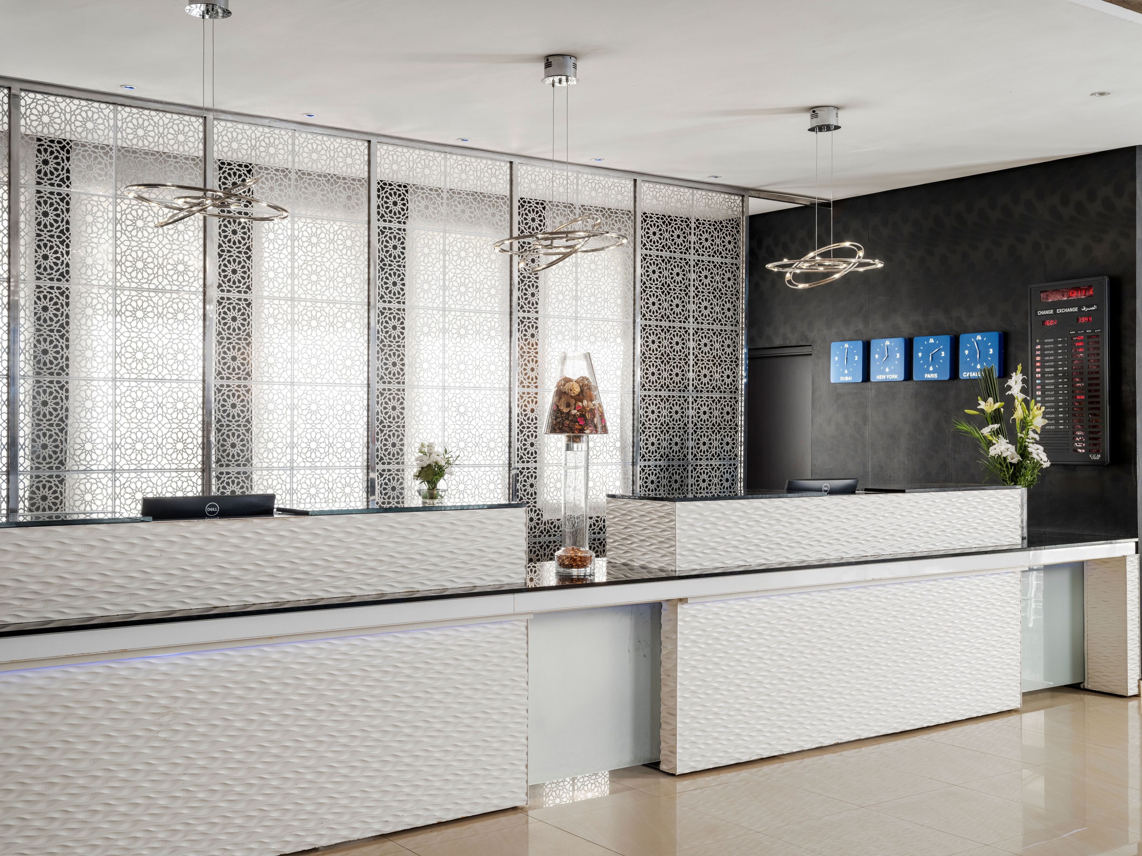 A modern reception desk with a patterned backdrop, a digital clock, and a decorative plant.