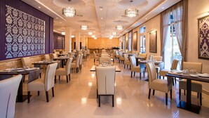 Een ruim restaurant met hoge plafonds, kroonluchters en diverse zithoeken.