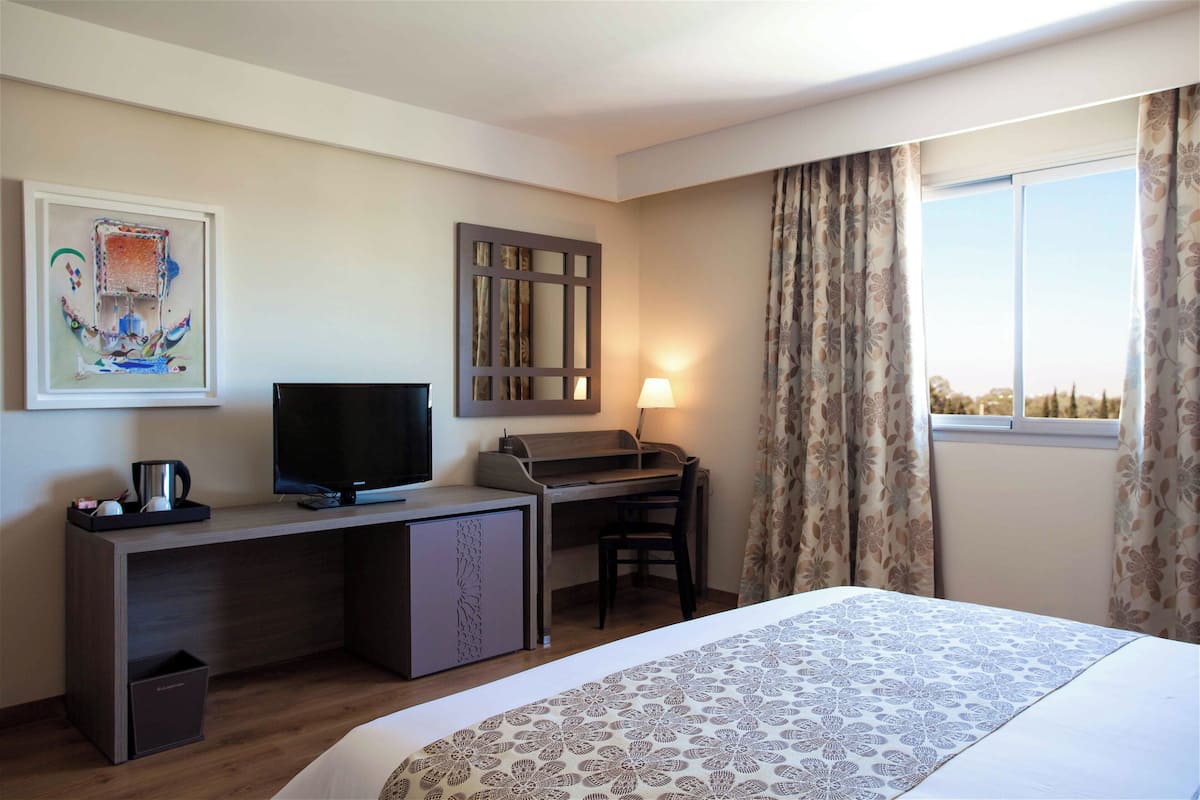 A hotel room with a bed, desk, television, and a window with curtains.