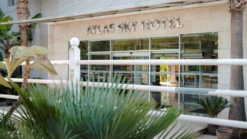 Exterior del Hotel Atlas Sky, con fachada moderna, amplias ventanas y una palmera en primer plano.