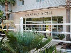 Exterior del Hotel Atlas Sky, con fachada moderna, amplias ventanas y una palmera en primer plano.