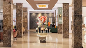 A modern lobby with marble columns, a reception desk, and a decorative floral arrangement.