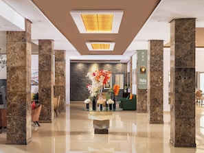 Un hall d’entrée moderne avec des colonnes en marbre, un comptoir d’accueil et une composition florale décorative.