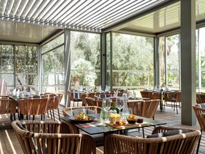 An outdoor dining area with wicker chairs and tables, surrounded by glass walls and large windows. - Sky Casa Airport (Nouaceur)