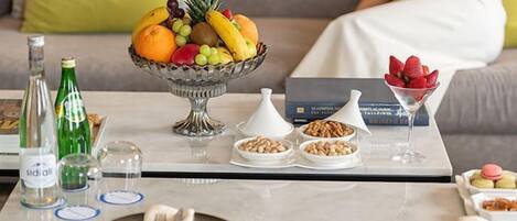 A dining table with a fruit bowl, bottles, glasses, and plates.