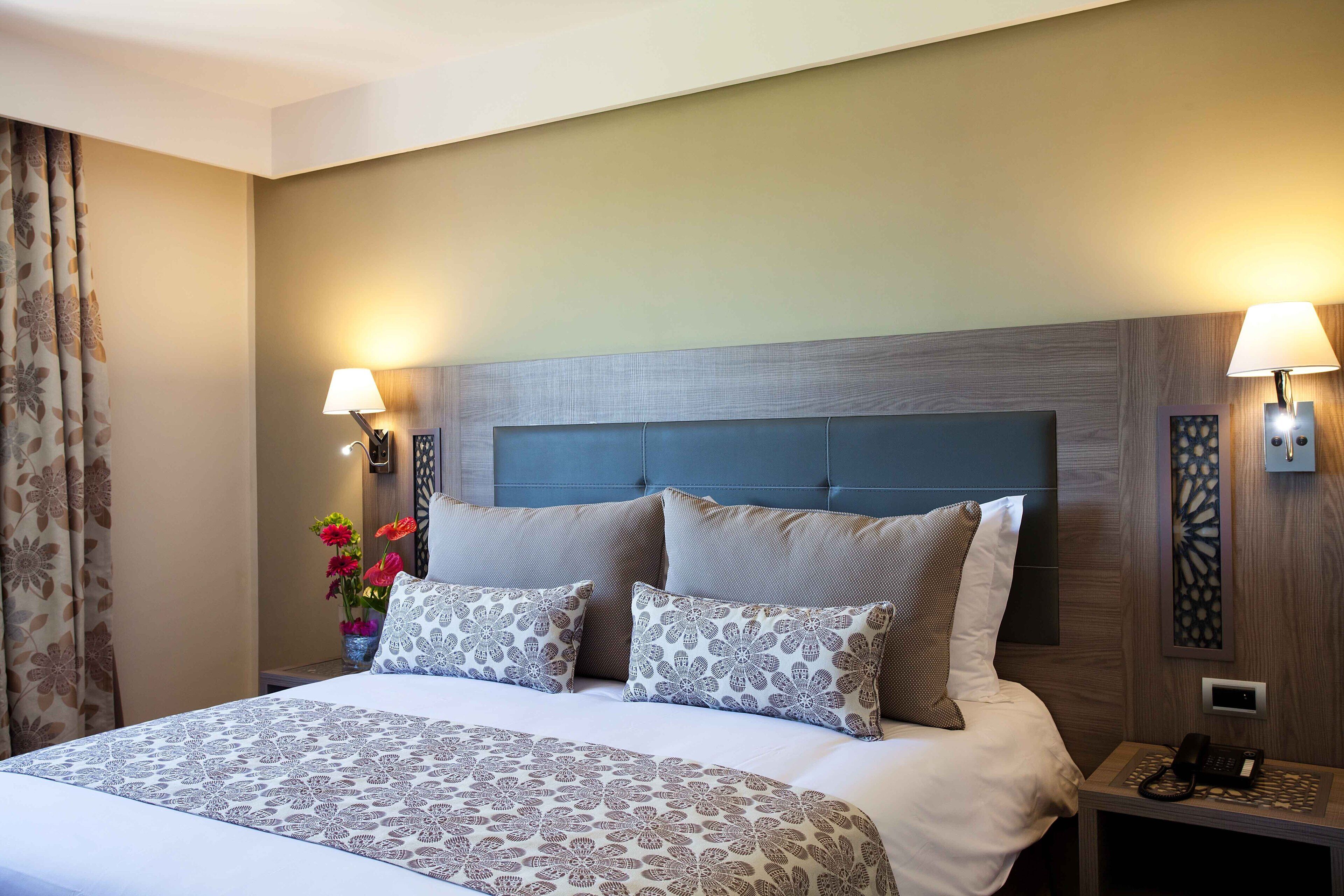 A hotel room with a large bed, two bedside lamps, a nightstand with a phone, and a decorative wall panel.