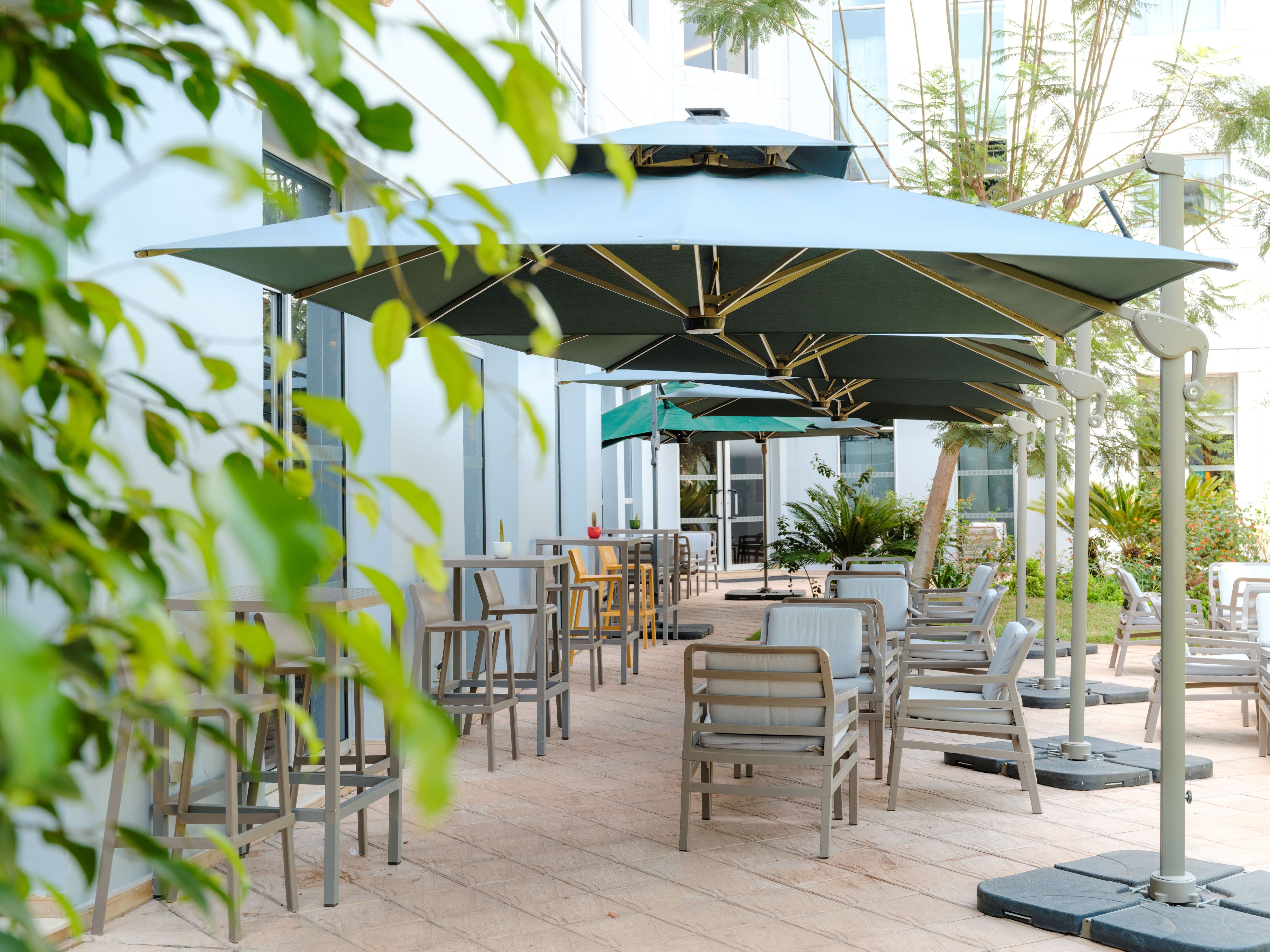 An outdoor seating area with tables and chairs, umbrellas, and a modern building in the background.