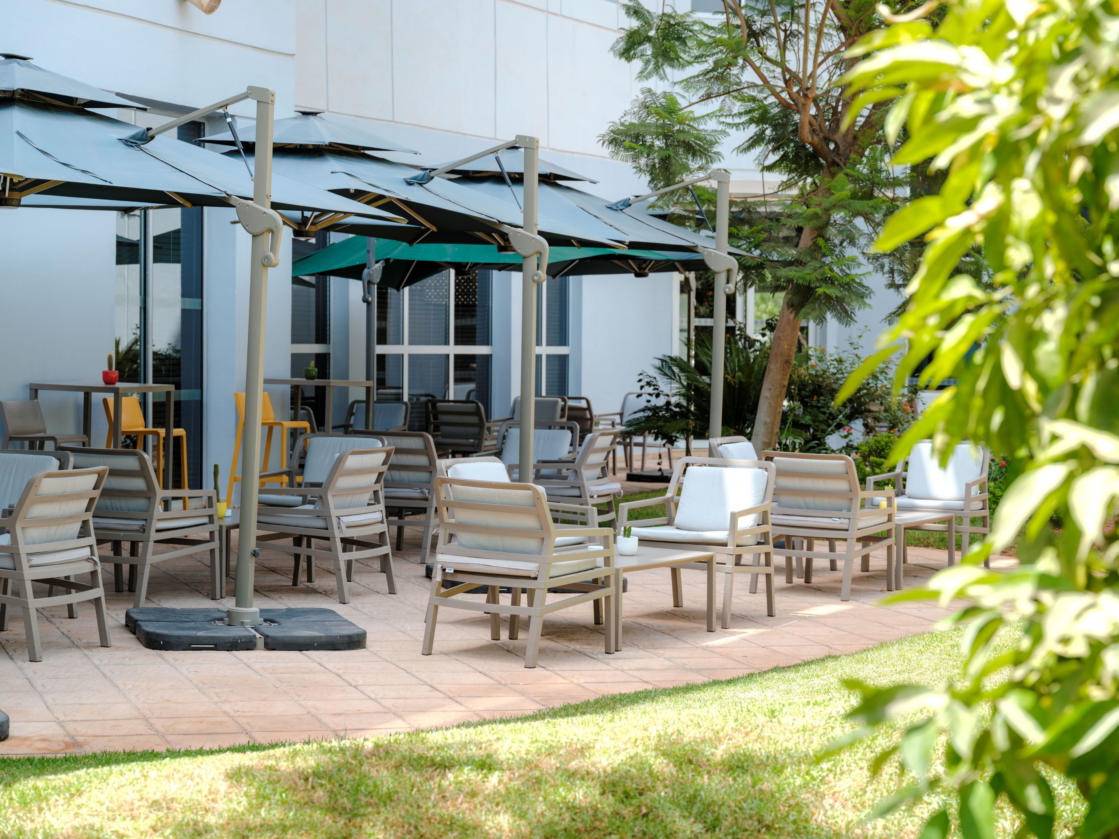 An outdoor seating area with tables and chairs, a covered section with umbrellas, and a building in the background.
