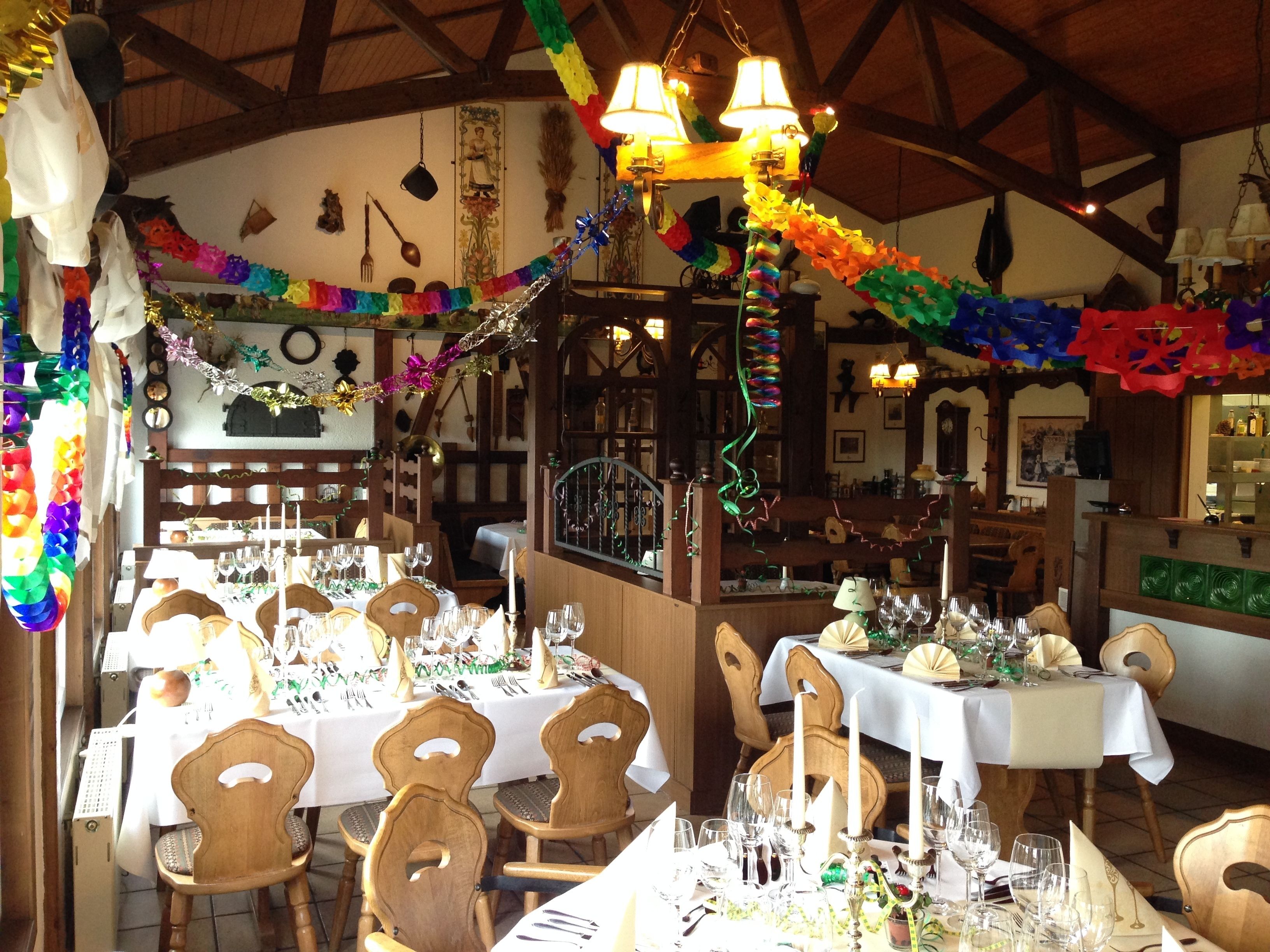 A restaurant with multiple tables set for dining, wooden chairs, and a variety of decorations including colorful streamers and hanging ornaments.