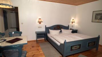 Un dormitorio con piso de madera, una cama con cabecera azul, dos mesitas de noche con lámparas, un escritorio con silla y un espejo.