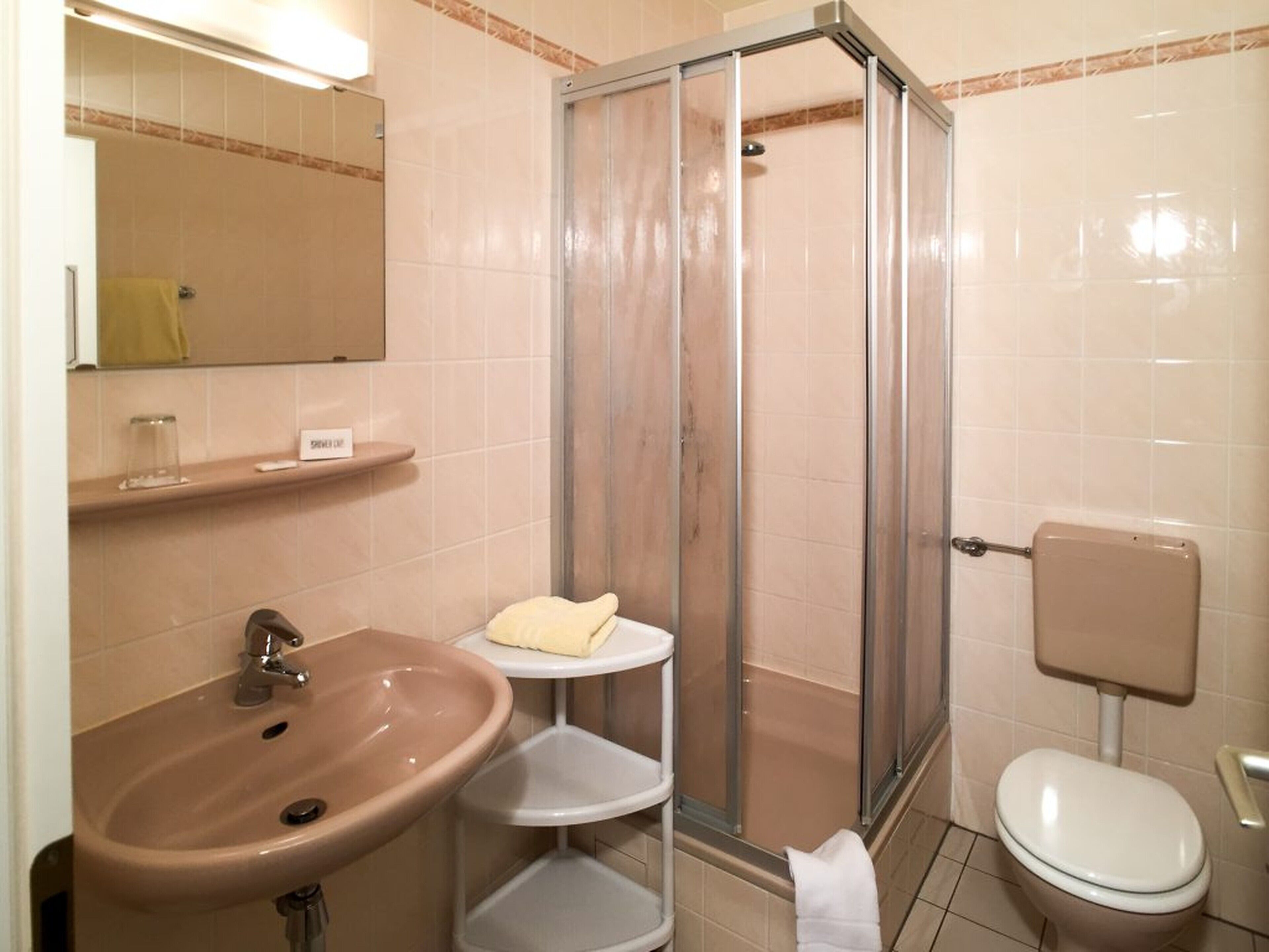 A bathroom with a sink, mirror, shower, toilet, and towel rack.