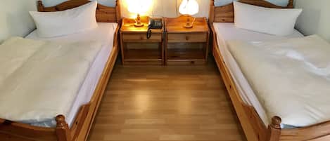 A room with two wooden beds, each with a nightstand and a lamp. There are two wall sockets and a power outlet on the wall.