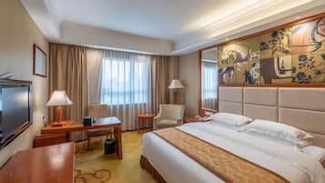 A hotel room with a large bed, a desk with a lamp, a chair, a TV, and a decorative wall.