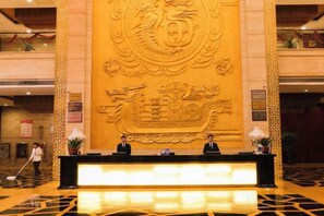 A reception desk with a large emblem in the background, a polished floor, and a person walking in the distance. - Xiongsen Holiday Villa (Chenzhou)