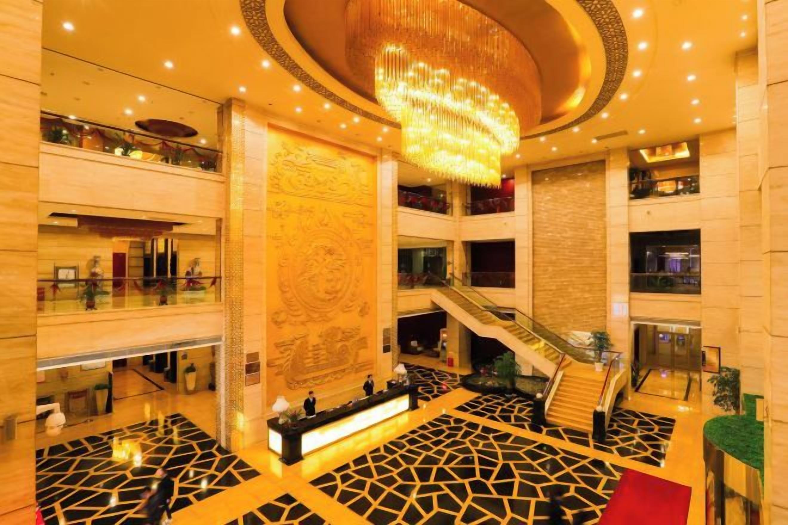 A spacious lobby with a central staircase, a reception desk, and a decorative wall.