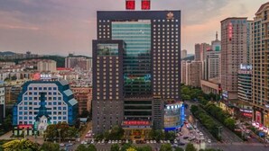 A high-rise building with a modern glass facade, surrounded by other buildings and a busy street. - Xiongsen Holiday Villa (Chenzhou)