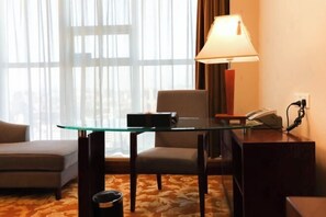 Habitación de hotel con un escritorio de vidrio, una lámpara, un teléfono y un cesto de basura.