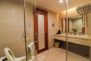 Un baño con cabina de ducha de vidrio, puerta de madera, lavabo con espejo y toallero.