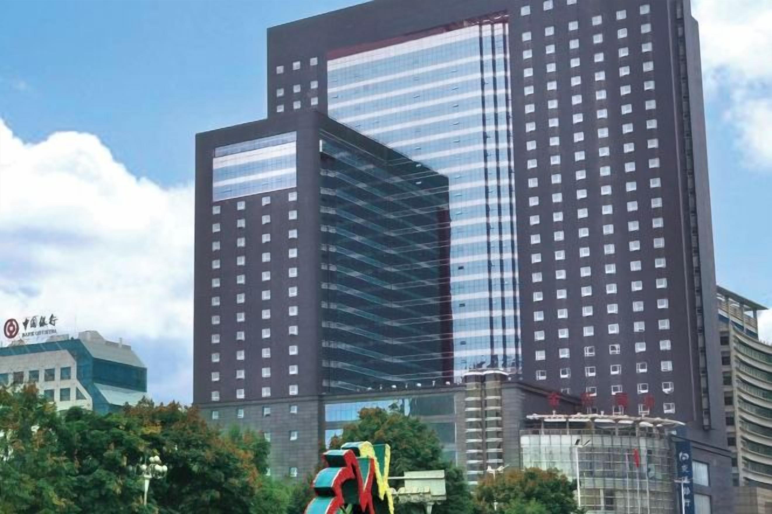Ein Hochhaus mit einer reflektierenden Glasfassade, mehreren Stockwerken und einer auffälligen Beschilderung auf der linken Seite.
