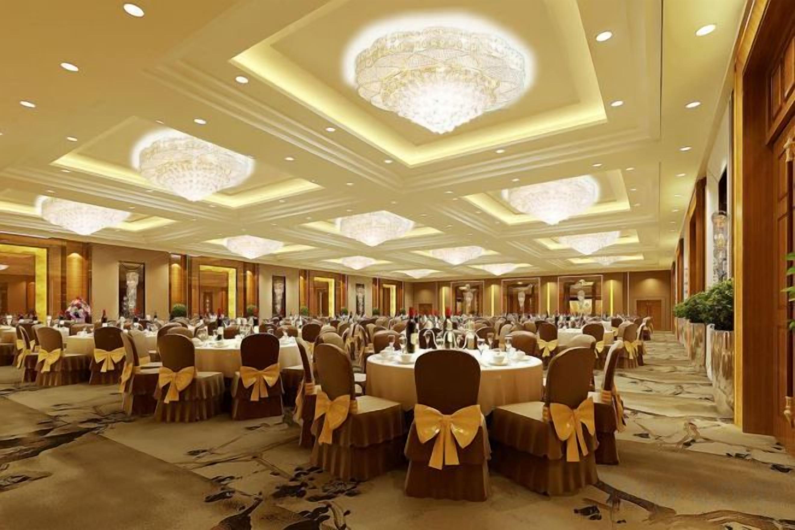 A banquet hall with round tables, chairs, and chandeliers.