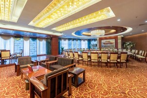 A hotel conference room with round tables, chairs, and a carpeted floor.