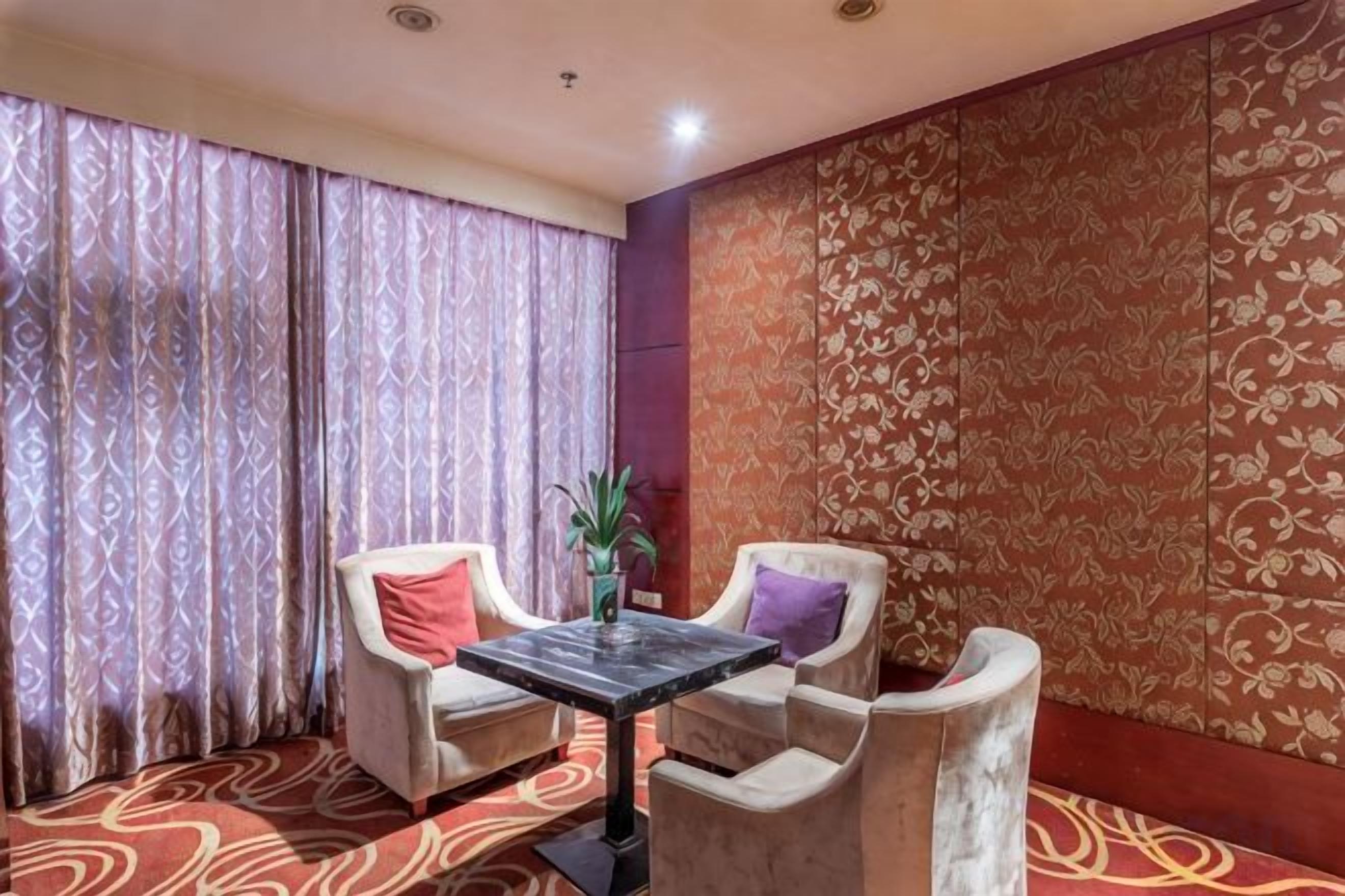 A room with a patterned carpet, two armchairs with cushions, a small table, and a potted plant.