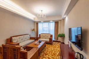 Habitación de hotel con sofá, una mesa de centro, televisor y alfombra estampada.