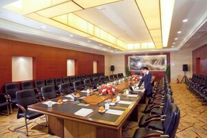 Un salón de conferencias con una larga mesa, varias sillas y una persona de pie junto a la mesa.