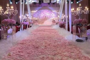 A wedding venue with a floral arch backdrop, a carpeted aisle, and chandeliers.