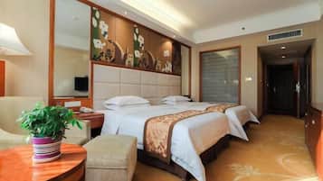 A hotel room with a large bed, a desk, a chair, a potted plant, and a large mirror.