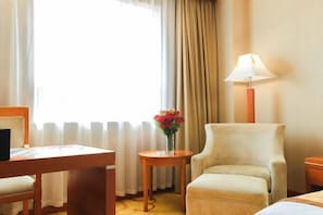 A hotel room with a bed, a chair, a small table with a vase of flowers, a lamp, and a window with curtains. - Xiongsen Holiday Villa (Chenzhou)