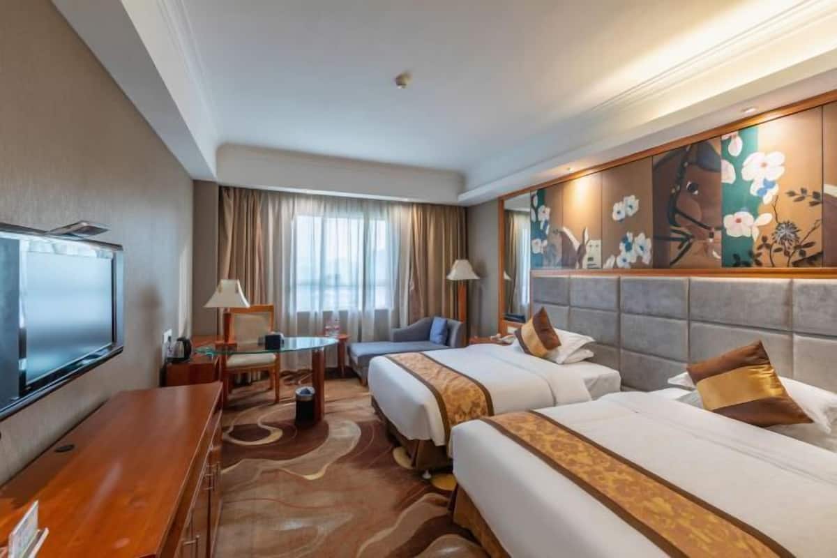 Habitación de hotel con dos camas, televisión, escritorio y ventana grande con cortinas.
