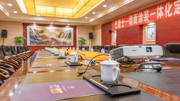 Un salón de conferencias con una larga mesa, sillas, un proyector y una pantalla para presentaciones.