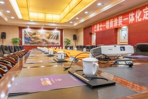 Un salón de conferencias con una larga mesa, sillas, un proyector y una pantalla para presentaciones.