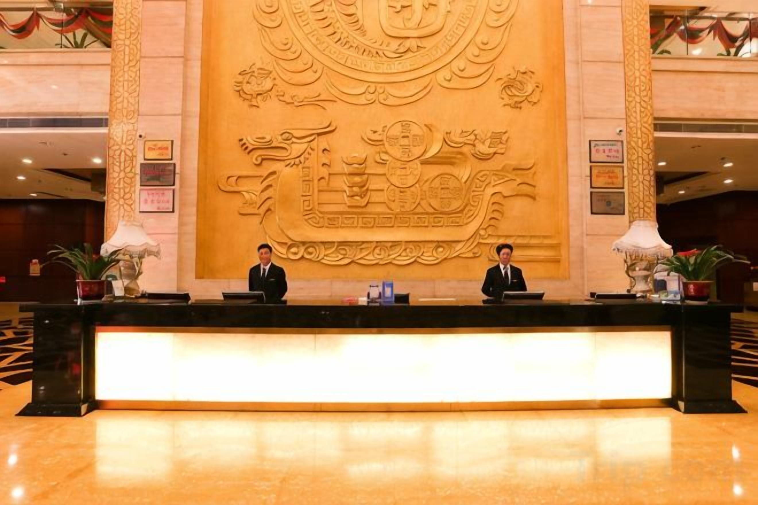 A reception desk with three staff members, a large decorative wall, and a polished floor.
