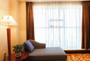 Ein Zimmer mit einer Couch, einer Lampe, einer Pflanze und einem Fenster mit Vorhängen.